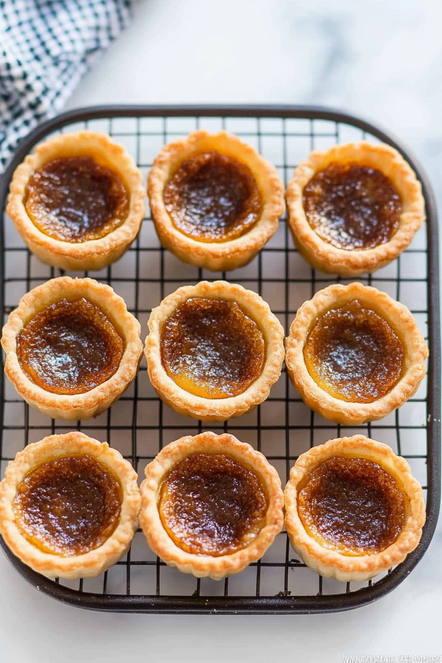 Freshly baked tarts cooling on a wire rack, with golden crusts and glossy caramelized filling.