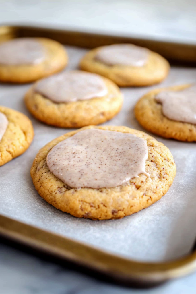 Soft homemade sugar cookies topped with creamy chai-spiced glaze on a baking sheet.