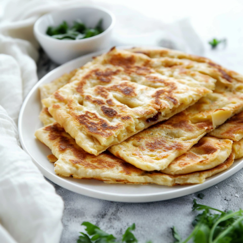 Stack of homemade stuffed flatbreads, golden brown with visible diced potato and melted cheese.