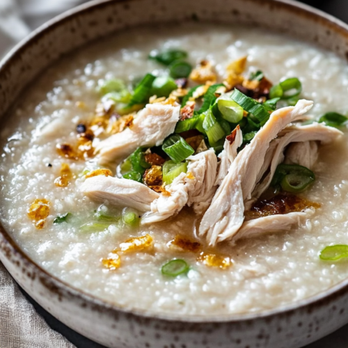 Homemade rice porridge presented with shredded chicken and herbs, highlighting its creamy consistency.