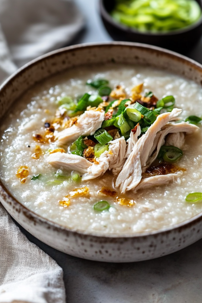 Homemade rice porridge presented with shredded chicken and herbs, highlighting its creamy consistency.