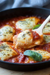 Golden cheese melting over pasta in tomato sauce, accented by fresh green herbs.