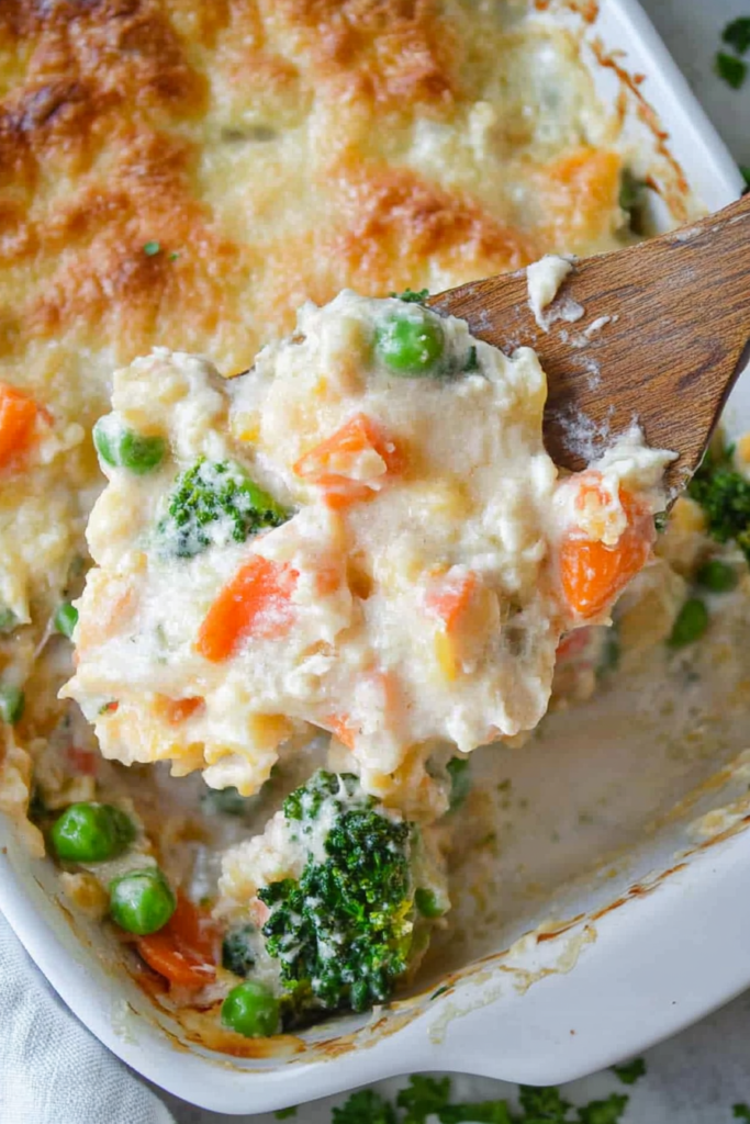 Close-up of colorful broccoli, carrots, peas, and corn nestled under melted cheese and browned topping.