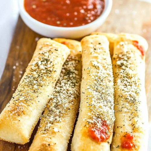 Freshly baked breadsticks arranged neatly on a rustic board with dipping sauce in the background