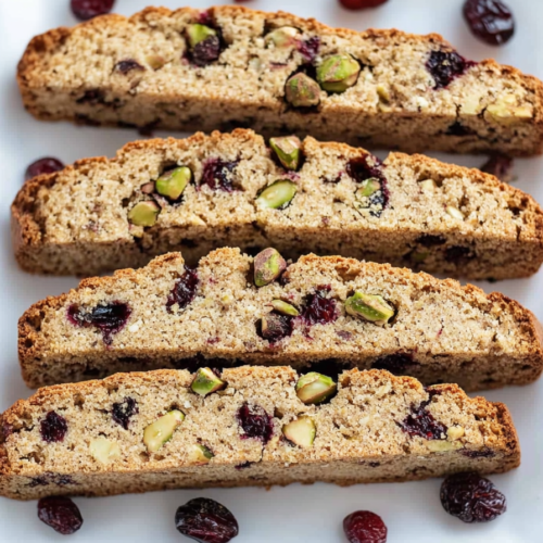 Close-up of crisp biscotti showing green nuts and red fruit pieces.