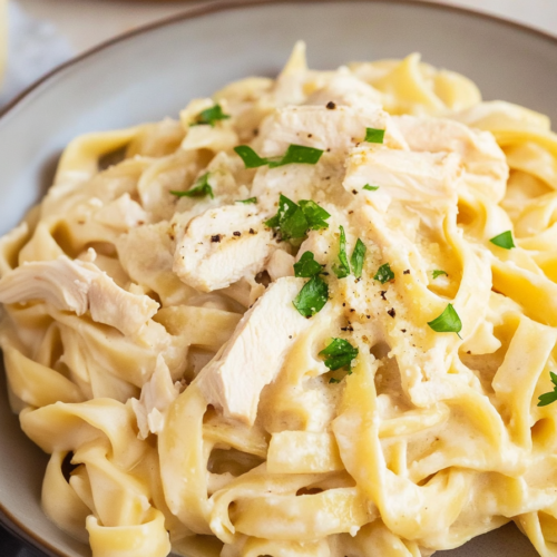 Close-up of pasta in rich cream sauce with tender chicken pieces and a sprinkle of black pepper.