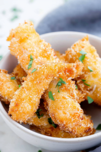 White ceramic bowl filled with golden-brown breaded chicken strips garnished with fresh herbs.