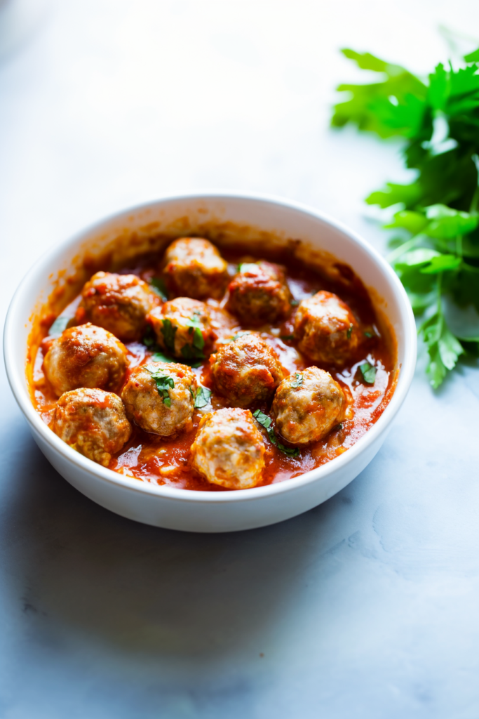 White serving bowl filled with baked meatballs, rich red sauce, and golden cheese