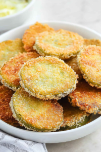 A shallow bowl filled with evenly breaded tomato slices, ready for dipping.