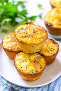 Freshly baked breakfast muffins with a soft center and cheesy top on a white plate