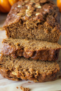 Moist spiced loaf bread topped with nuts and sliced on a wooden board.