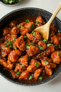 Pan of saucy chicken topped with chopped green onions and cilantro, ready to serve with a wooden spoon.