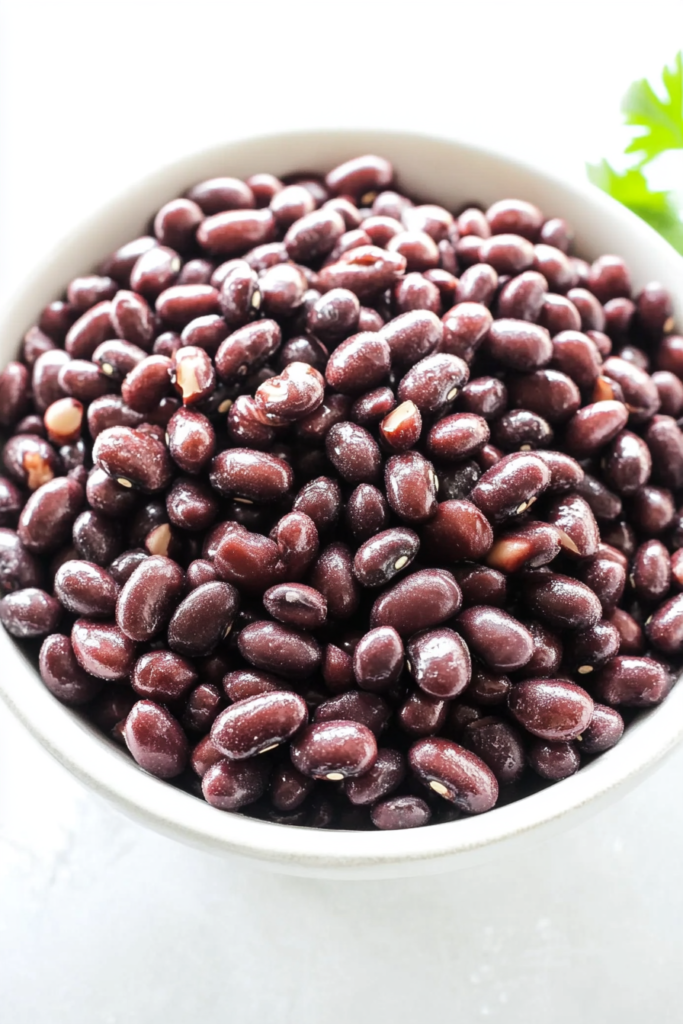 Close-up of glossy adzuki beans served in a white bowl, topped with fresh parsley leaves.
