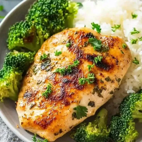 Plated chicken breast with a crisp sear, accompanied by tender broccoli florets and a side of white rice.