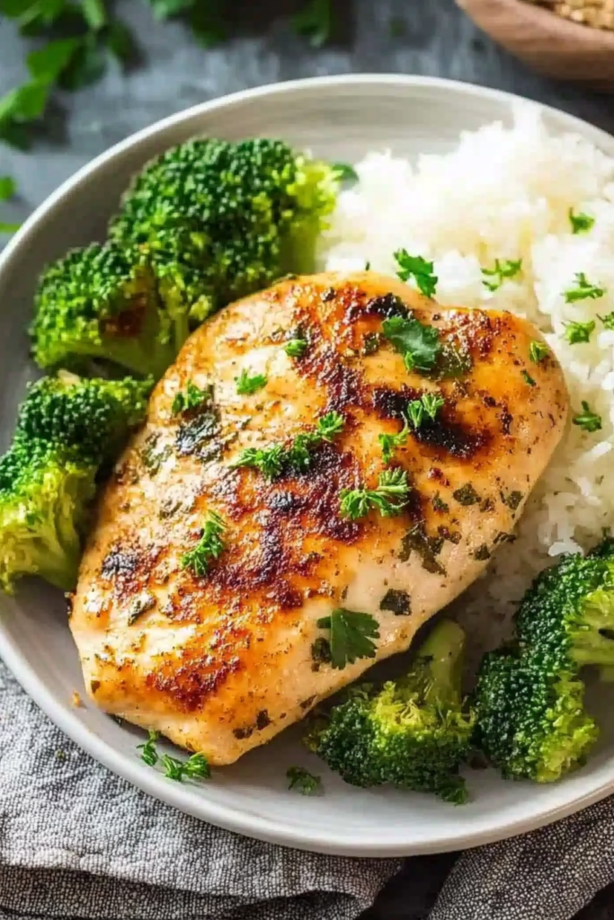 Plated chicken breast with a crisp sear, accompanied by tender broccoli florets and a side of white rice.