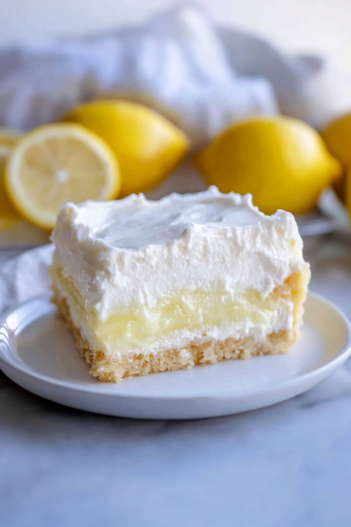 Slice of creamy lemon icebox cake with whipped topping and a buttery crust on a white plate.
