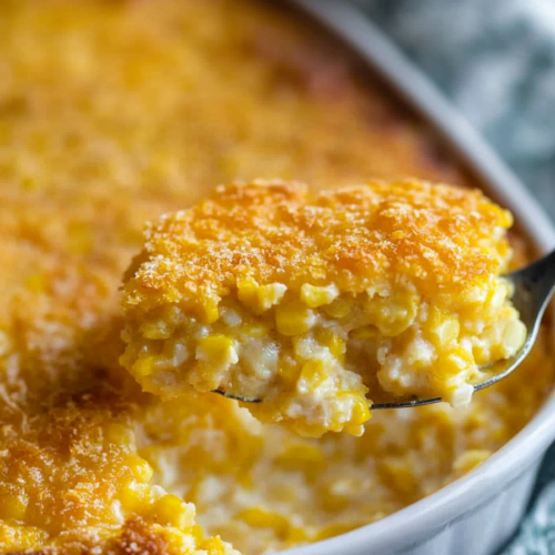 Golden corn pudding with a crisp top layer, scooped fresh from a ceramic baking dish.