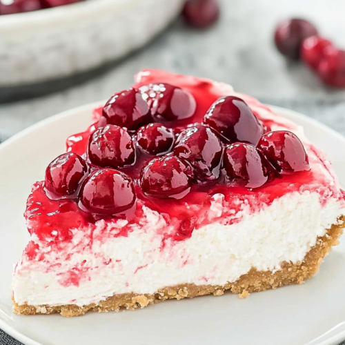 Rich cheesecake slice with crumbly crust and vibrant cherry layer glistening on top.