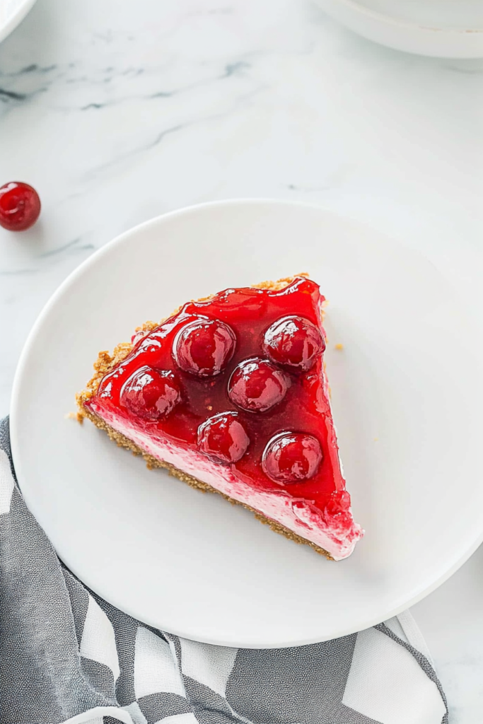 Slice of creamy cheesecake with glossy cherry topping on a graham cracker crust.