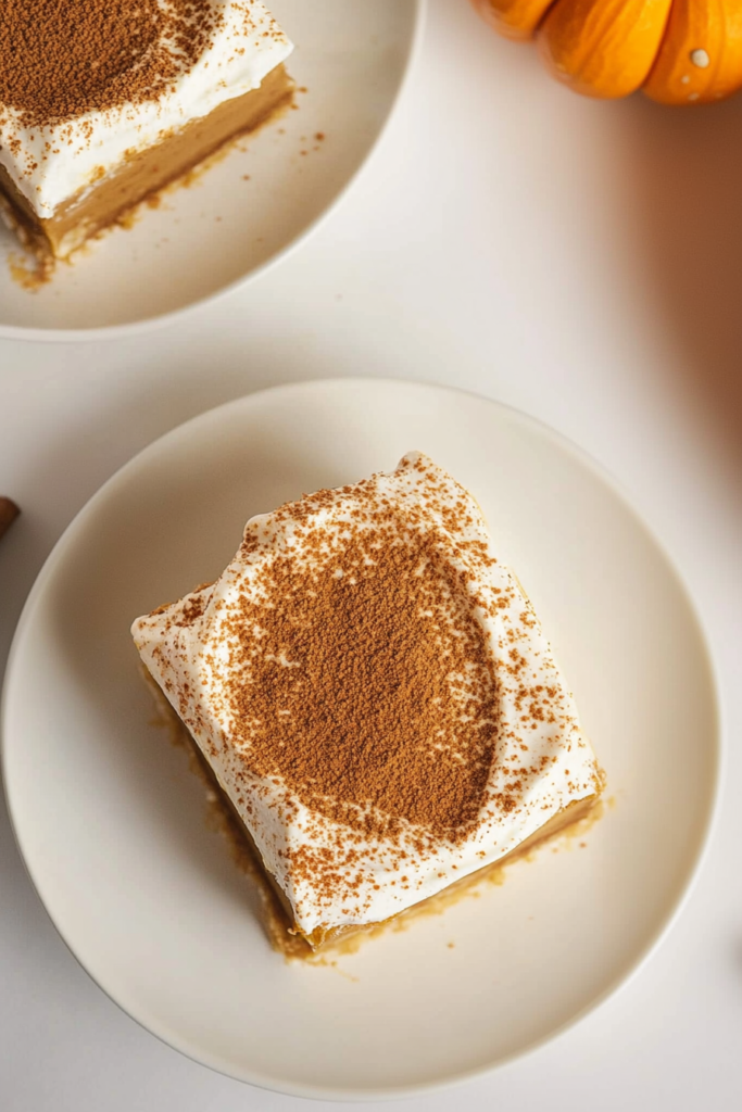 Slice of layered pumpkin dessert topped with whipped cream and cinnamon.