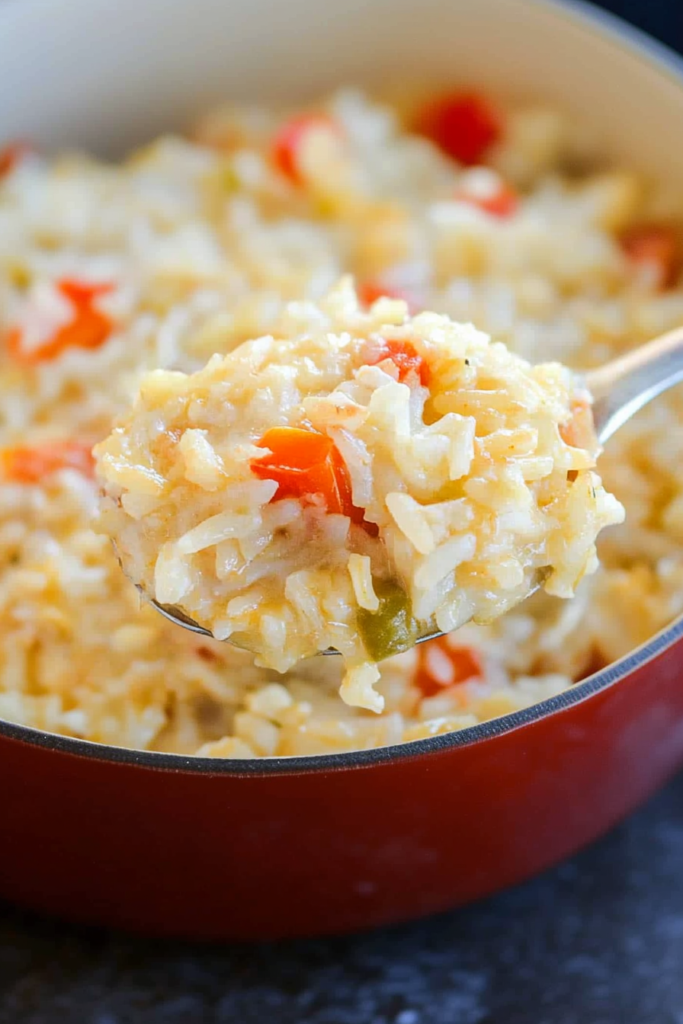 Baked rice dish showing melted cheese and diced vegetables in a serving spoon.