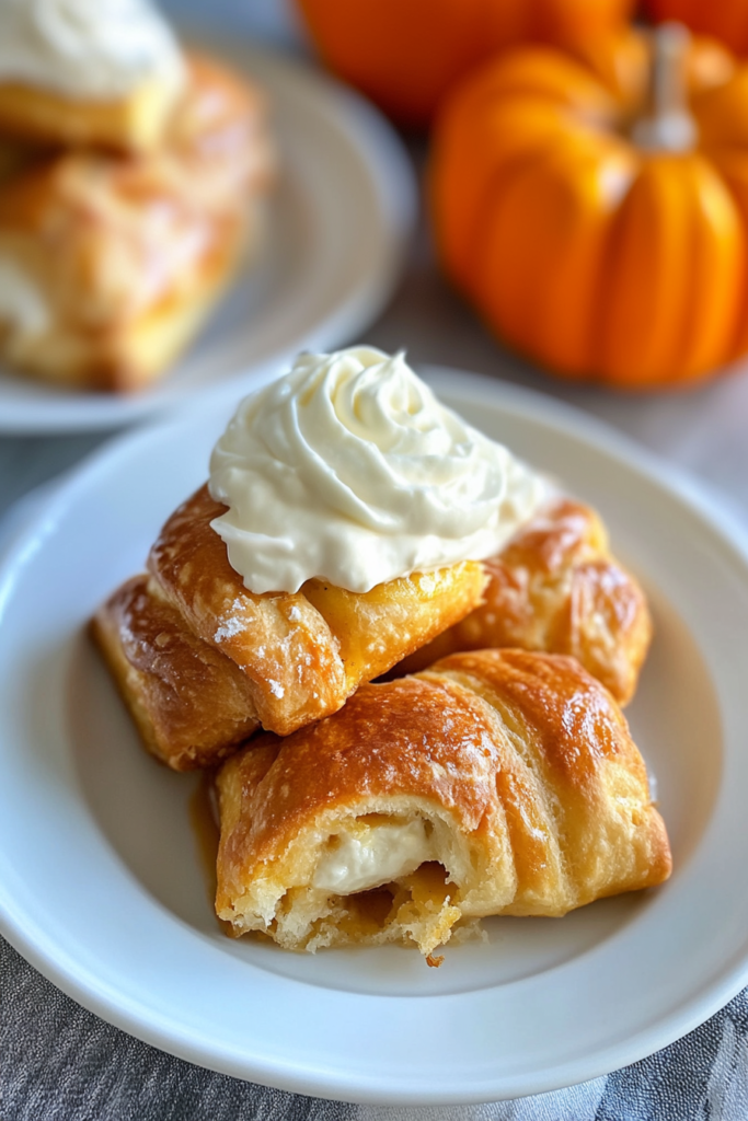 Golden baked pastry bites filled with pumpkin and cream cheese, topped with a swirl of whipped cream.