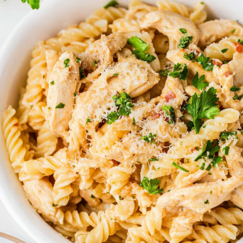 Close-up of tender chicken pieces mixed into spiral pasta with a rich, cheesy cream sauce.