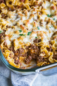 Glass baking dish filled with saucy noodles and beef, finished with a crisp cheese topping.
