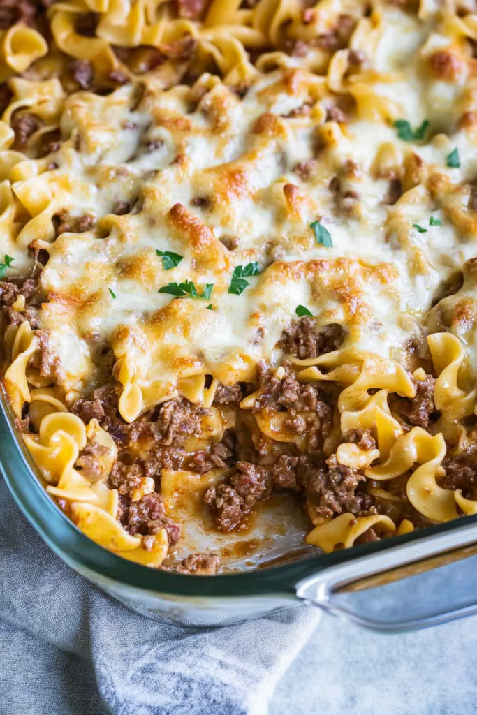 Glass baking dish filled with saucy noodles and beef, finished with a crisp cheese topping.