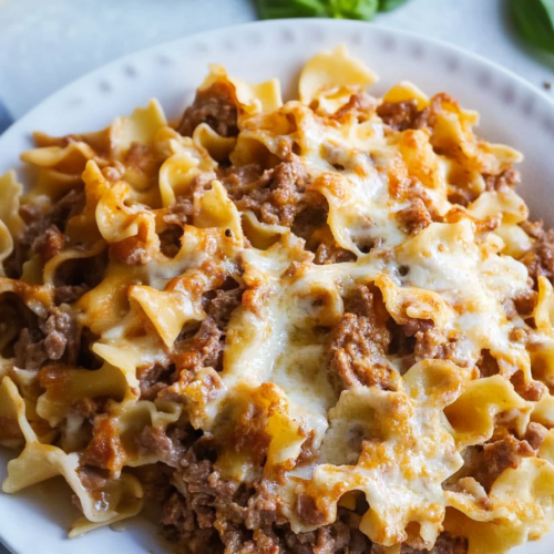 Hearty casserole portion being scooped out, with layers of noodles, beef, and golden cheese visible.