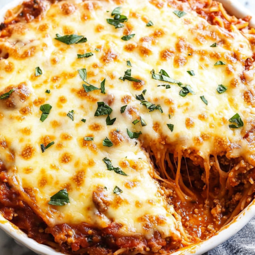 Slice removed from a cheesy pasta bake revealing layers of sauce and noodles.