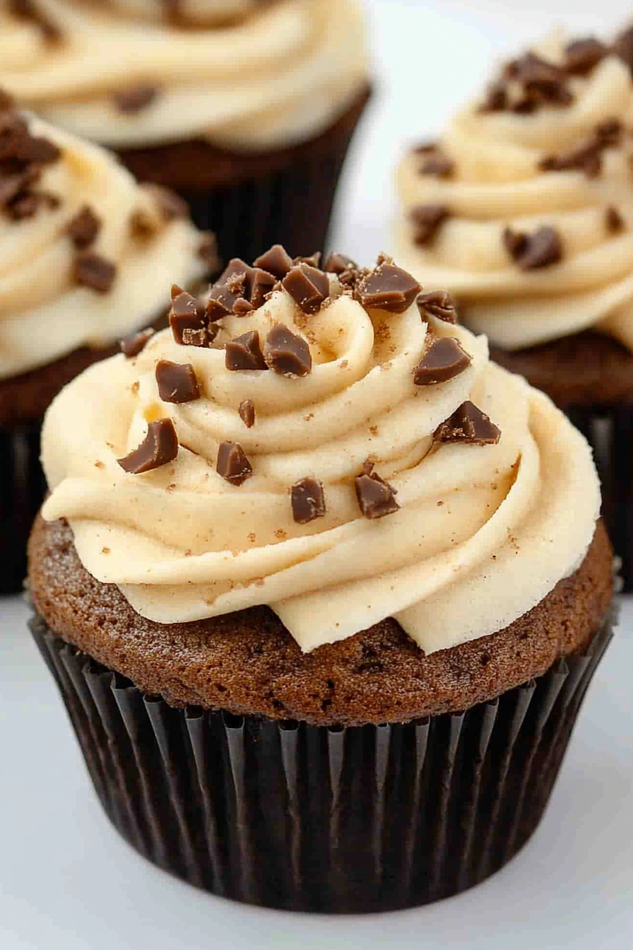 Close-up of rich mocha cupcake in a dark paper liner, topped with decorative frosting.