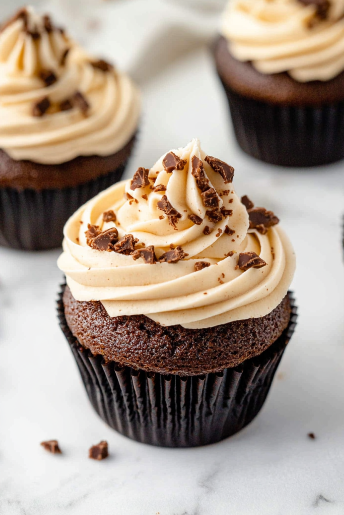 Dessert display of frosted chocolate cupcakes, slightly blurred in the background.