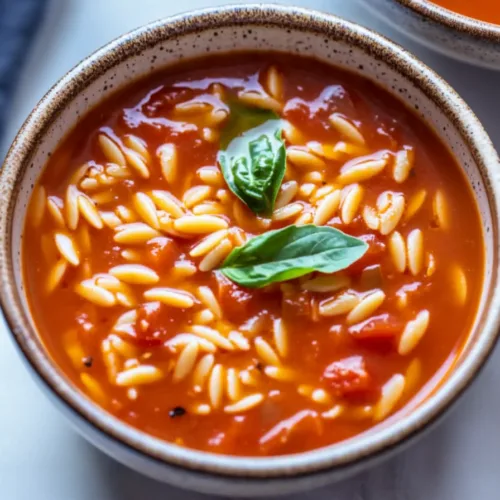 Warm red tomato broth with small pasta and a basil leaf in a rustic bowl.