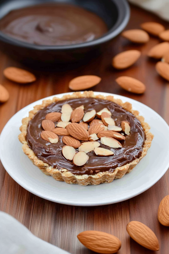 Homemade tart with smooth chocolate surface and nutty topping, presented on a wooden table.