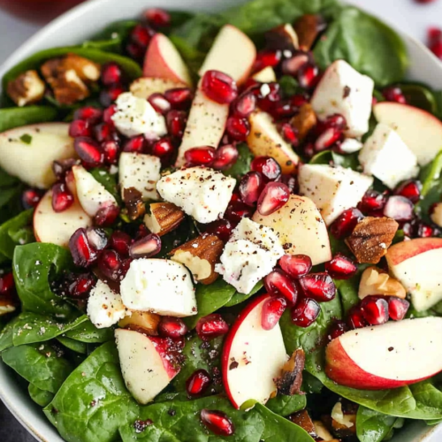 Fresh salad with chopped apples, pomegranate seeds, and pecans over leafy greens