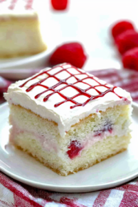Slice of layered sponge cake with pink fruit filling and white frosting decorated with red icing.