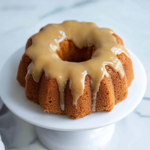 Golden bundt-style cake drizzled with glossy caramel glaze on a white cake stand.
