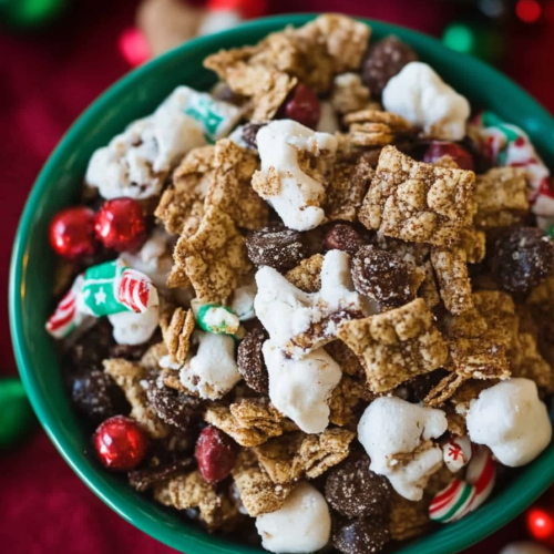 Bowl of festive snack mix with red and green candy-coated chocolates and sugar-dusted popcorn.
