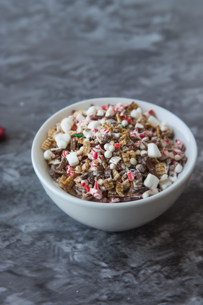 Colorful holiday snack mix with cereal, pretzels, popcorn, and festive candies in a serving bowl.