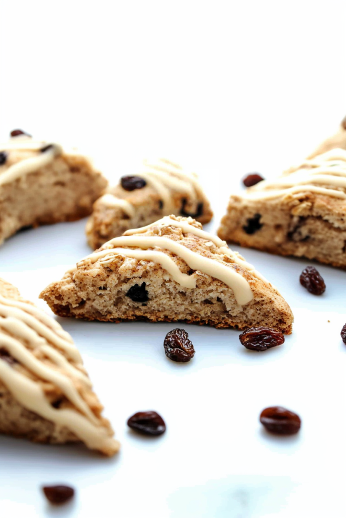 Triangular baked scones drizzled with smooth beige glaze, highlighting oats and raisins.