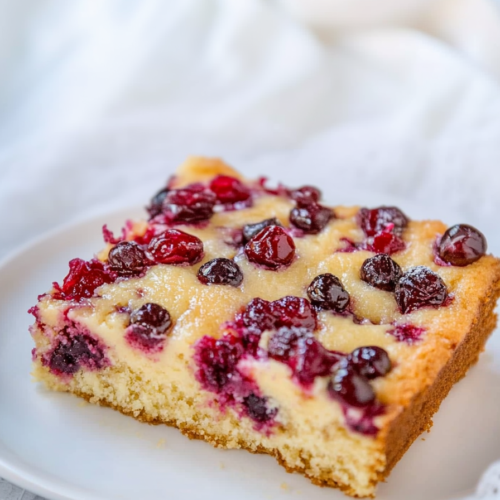 Final presentation of cake slice on a white plate, with vibrant cranberries and blueberries baked in.