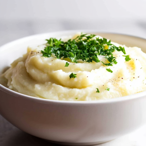 Homemade mashed potatoes with soft texture and herb garnish on top.