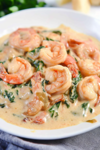 Close-up of pink shrimp coated in velvety cream sauce, garnished with fresh greens.