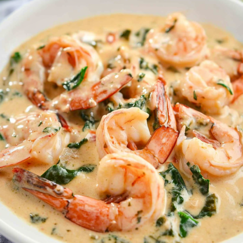 Plated shrimp in a creamy garlic sauce with wilted spinach and herbs.