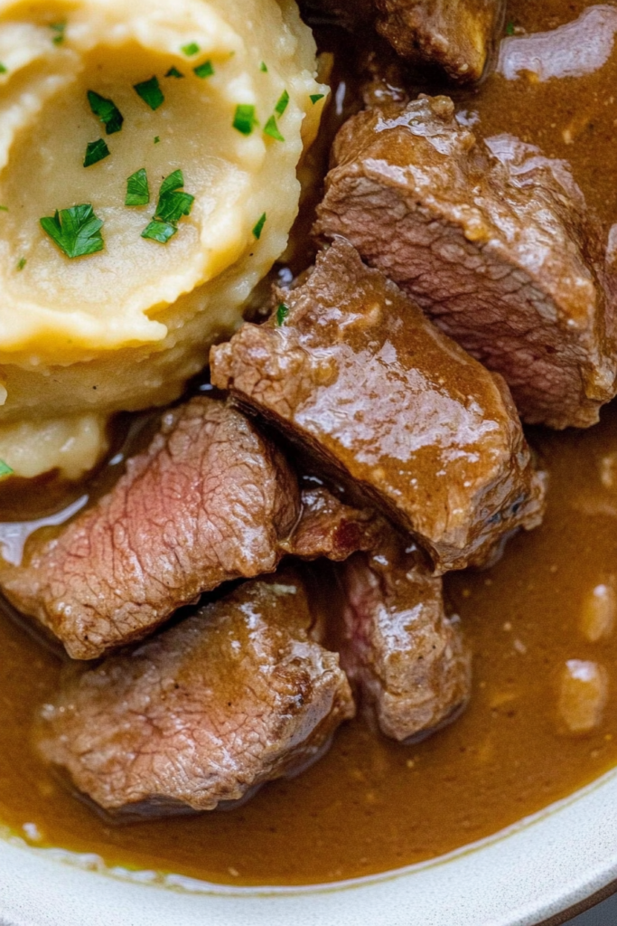 Comfort food meal featuring tender beef in gravy and creamy mashed potatoes on a white plate.