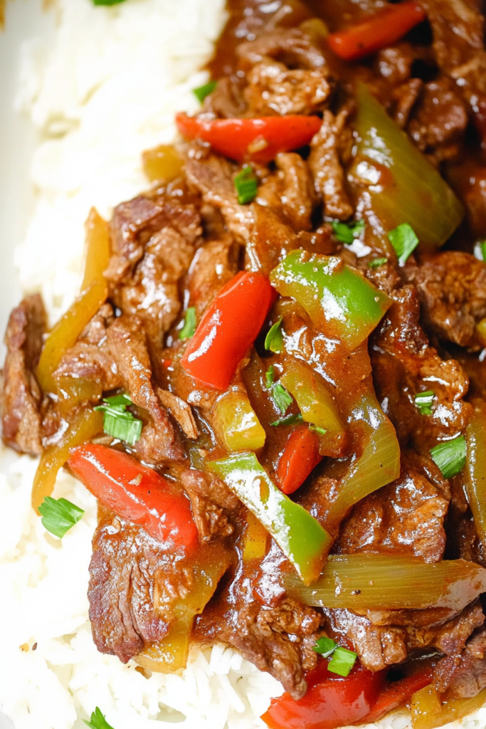 Hearty beef and pepper dish spooned over fluffy rice, garnished with chopped green onions.