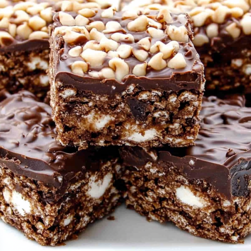 Stacked chocolate cereal bars topped with glossy chocolate and chopped peanuts.