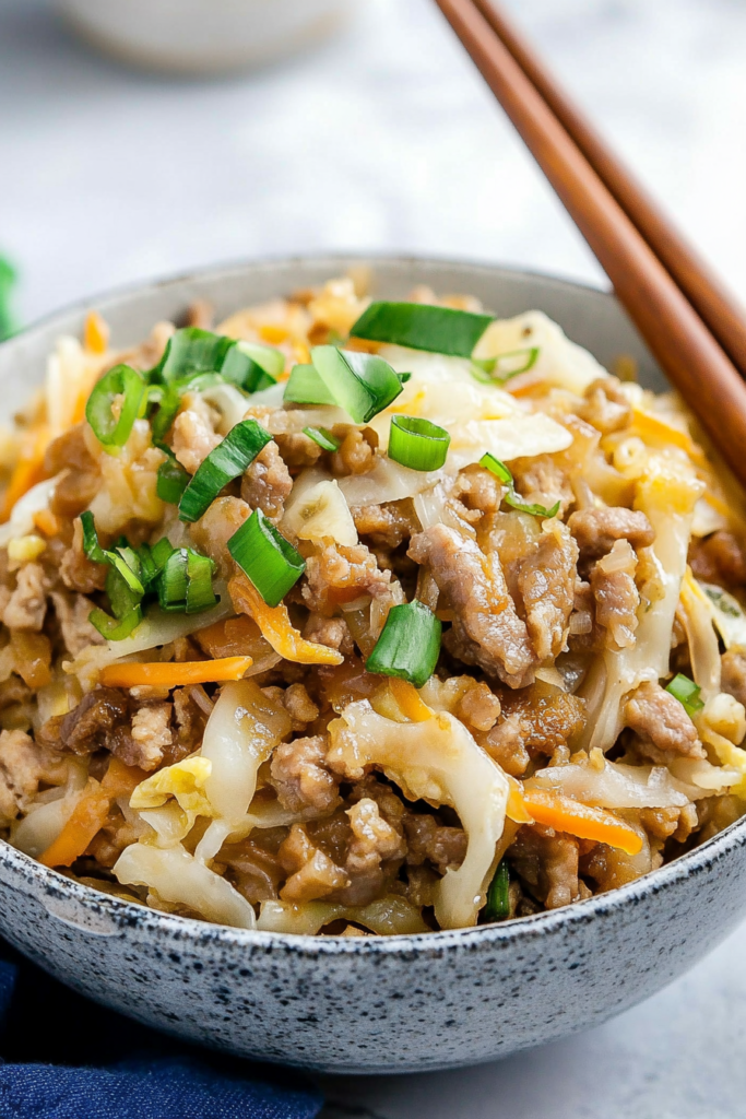 Close-up of a hearty bowl of sautรฉed vegetables and protein, ready to eat with chopsticks.