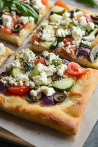 Golden-brown pizza squares with colorful Mediterranean toppings and fresh basil leaves